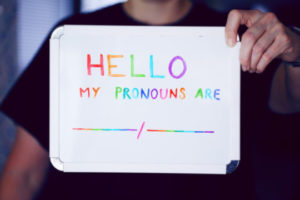 Photo of person holding up sign reading "Hello, my pronouns are __/__"