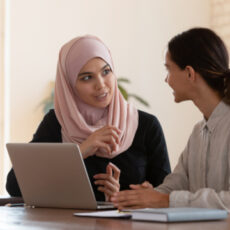 Photo of two people talking and using laptop