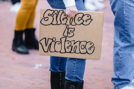 photo of protester holding sign "silence is violence"